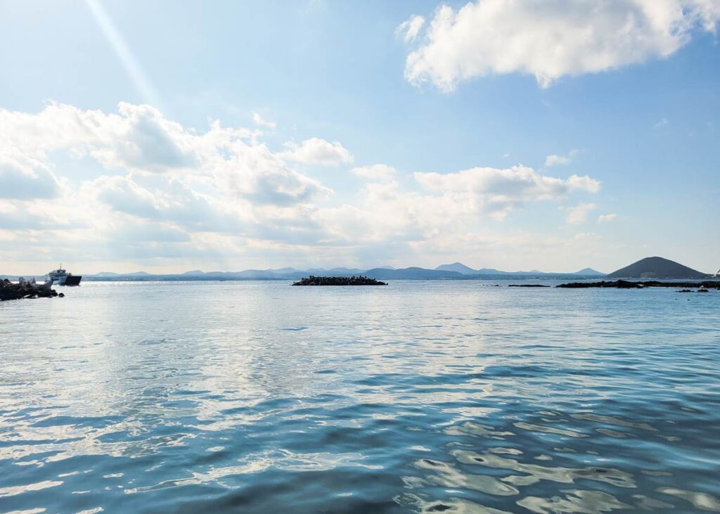 view of the east coast of jeju island from the udo island ferry with seongsan ilchulbong in the distance and blue waters